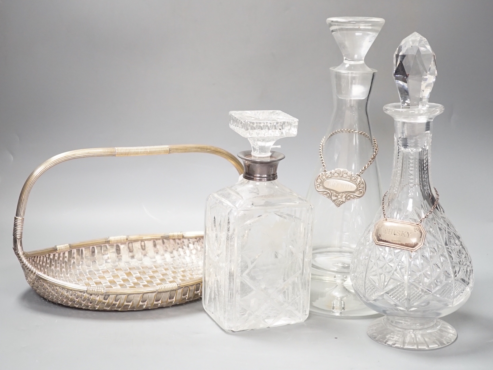 A silver topped decanter together with two other assorted decanters, a silver whisky label and a silver plated basket